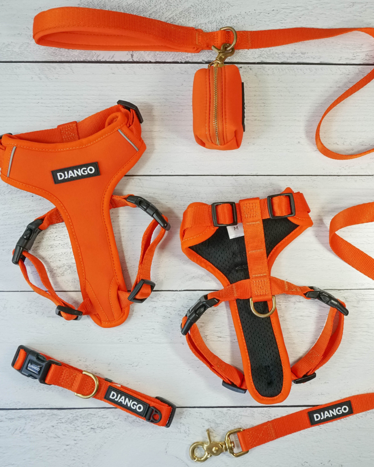Front and back lay flat views of DJANGO Adventure Dog Harness in Sunset Orange on light wooden surface with matching leash, collar, and poop bag holder.