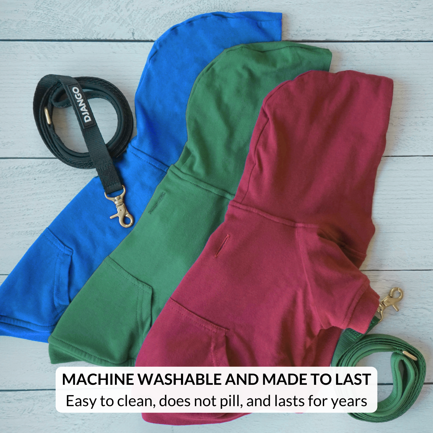 Three dog hoodies in blue, green, and red with matching leashes on a wooden surface.