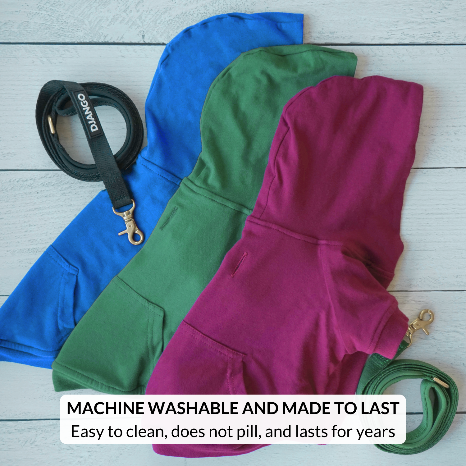 Three hoodies in blue, green, and purple with matching leashes on a wooden surface.