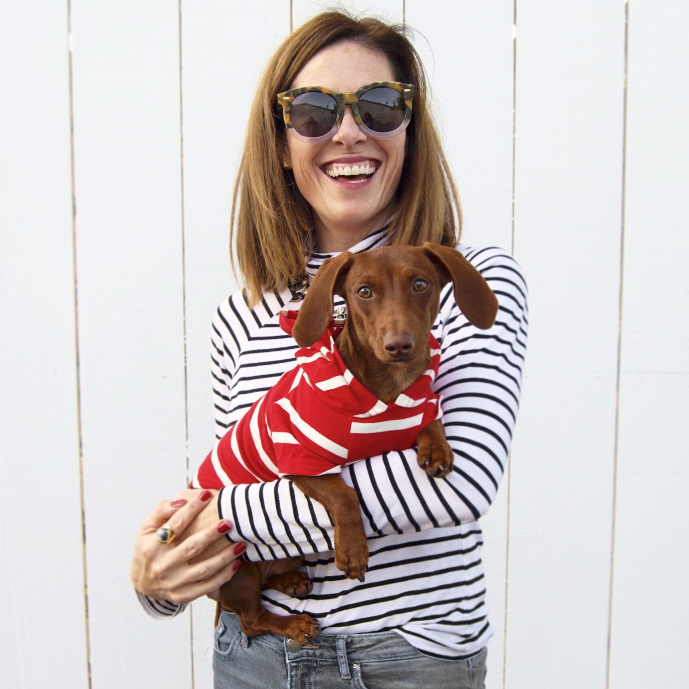 Happy dog mom holding mini dachshund who is wearing a soft red striped dog hoodie outdoors