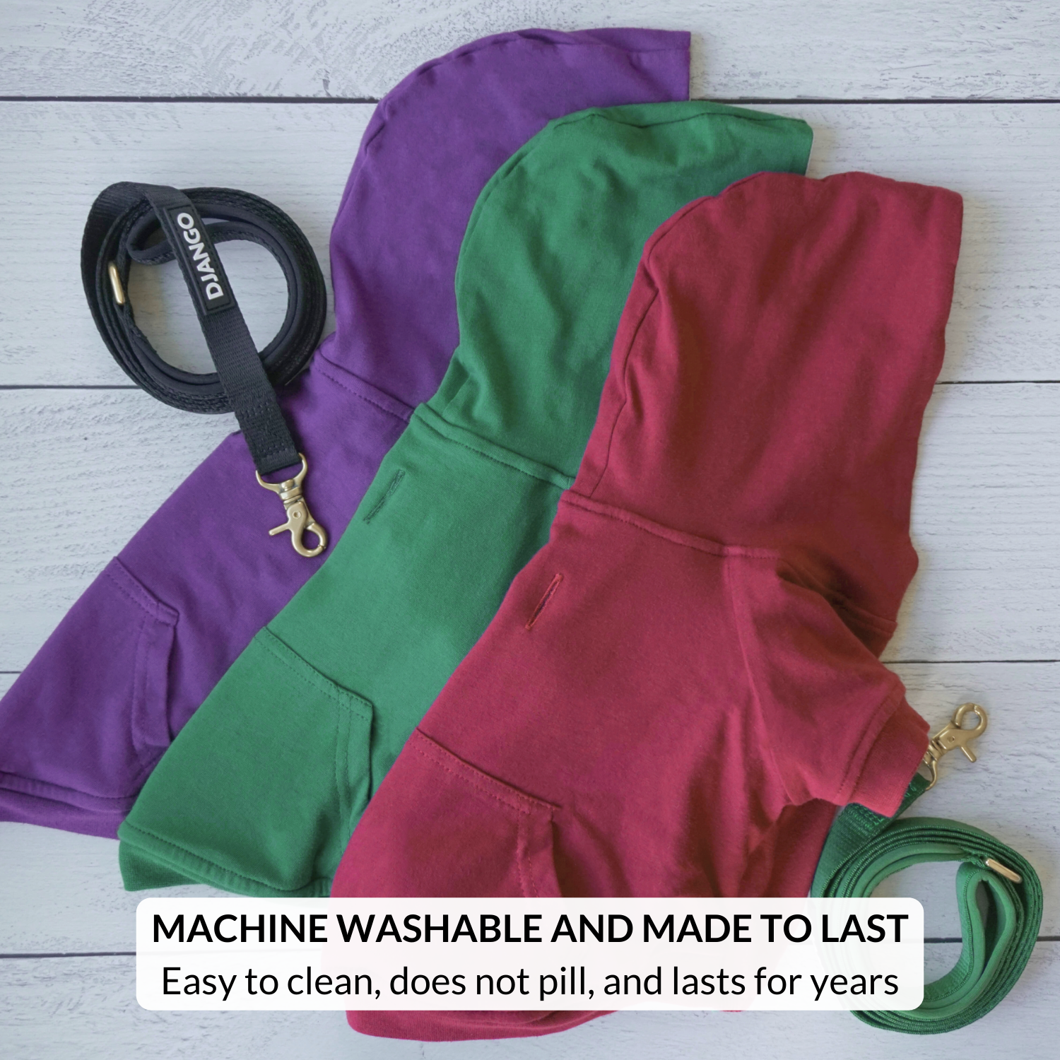 Three hoodies in purple, green, and red with matching leashes on a wooden surface.