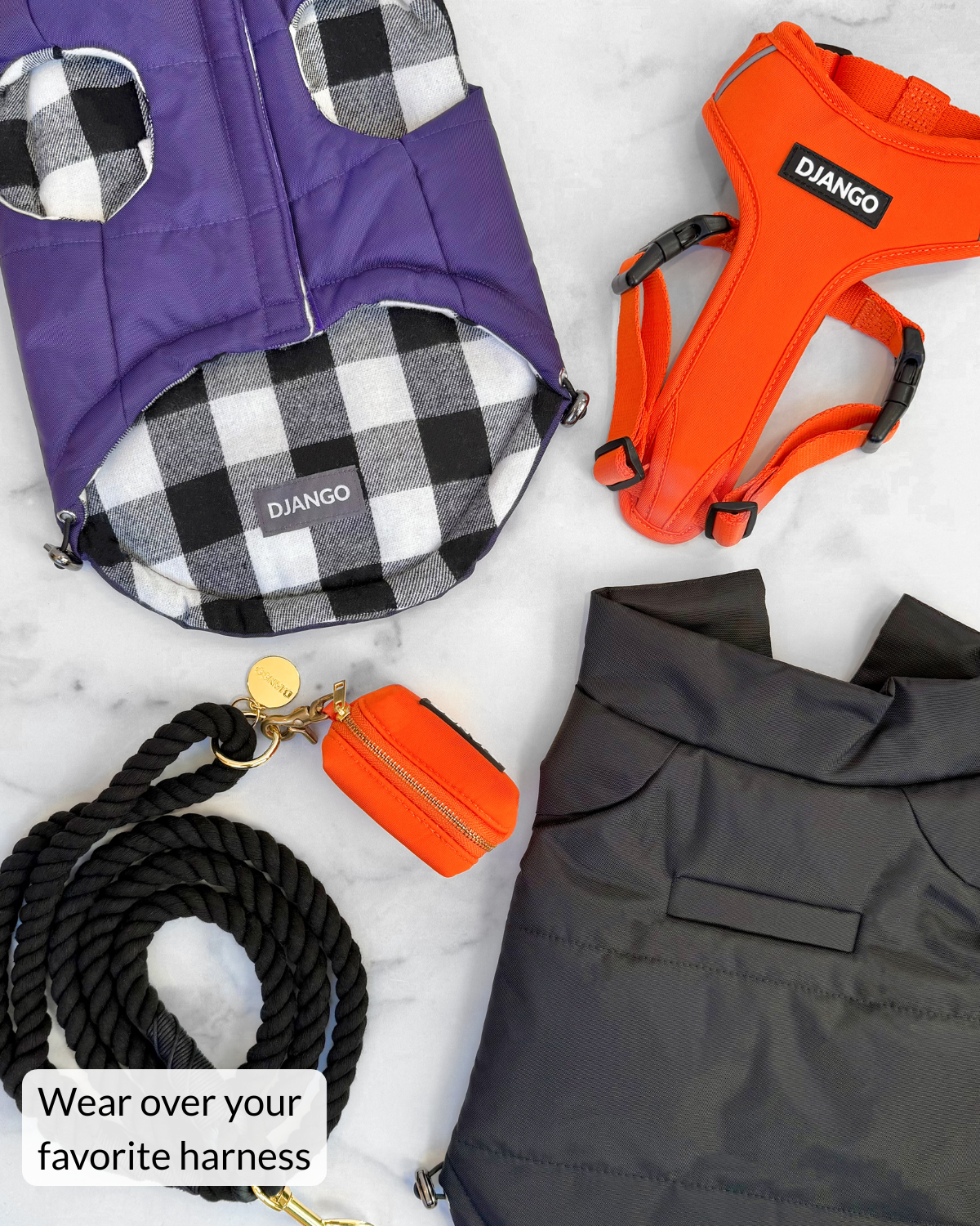 A styled flat-lay of dog coats and dog walking accessories on a white marble background, including a purple dog vest with black-and-white buffalo plaid trim, an orange harness labeled DJANGO, a black rope leash for dogs, an orange poop bag holder, and black puffer jacket with harness hole. A text overlay reads 'Wear over your favorite harness'.